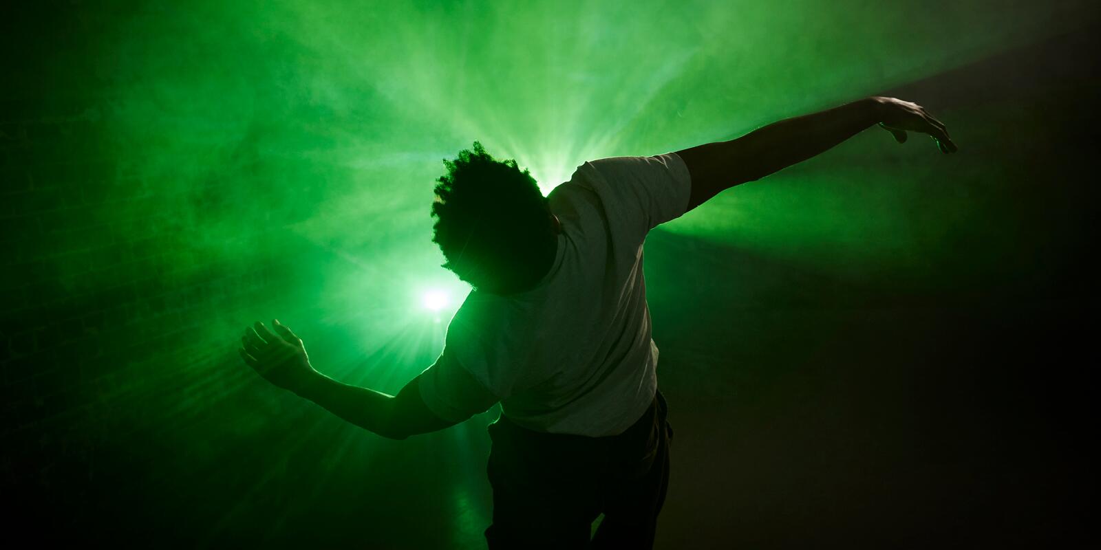 A dancer in movement silhouetted against green light