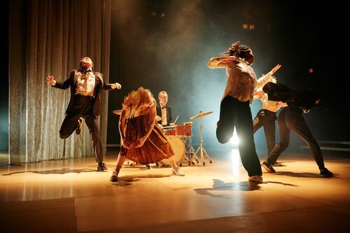 Four dancers in movement on stage with Conor Guilfoyle at a drumset in the centre