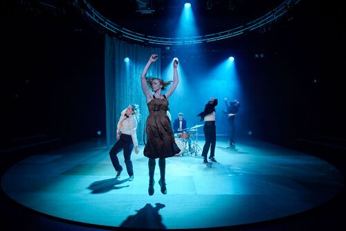 Four dancers in movement in blue light with Conor Guilfoyle at a set of drums in the centre