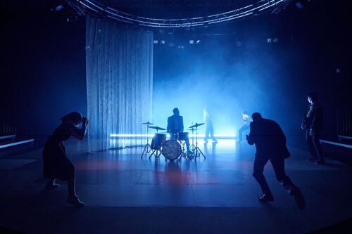 Four dancers in silhouette spread in a circle around a drummer at a drum-set