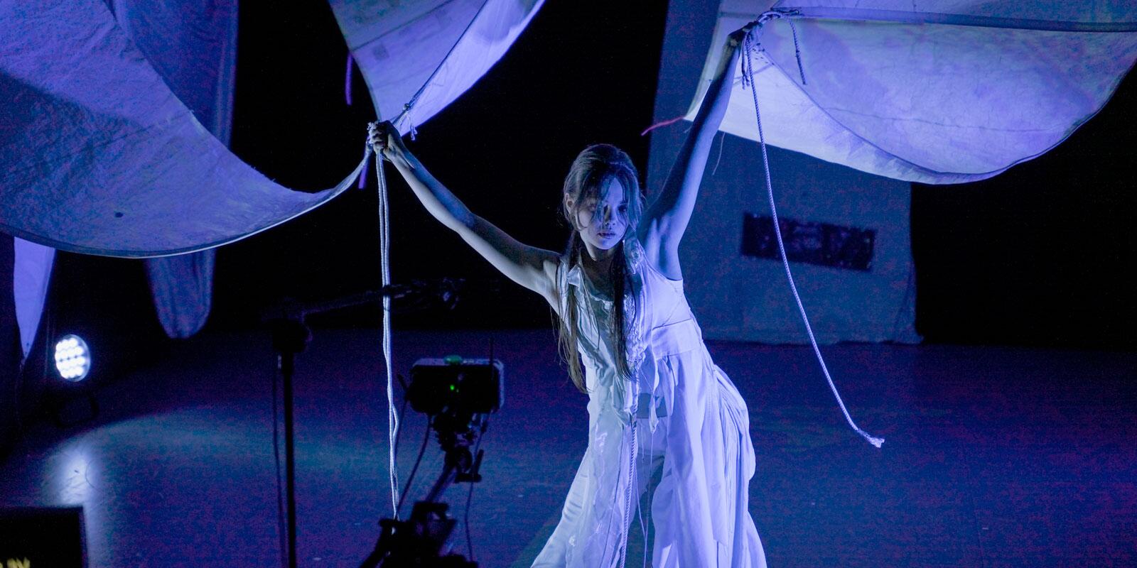 Rosie Stebbing in movement holding the ends of sails above her head