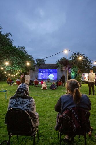 Two people seen from behind, seated looking at a handball alley with projections cast on its wall