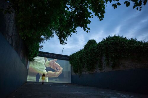 A single figure standing in an empty handball alley with projections cast on the back wall