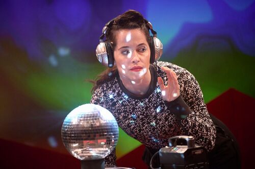 Stephanie Dufresne listening to headphones behind a shining disco ball