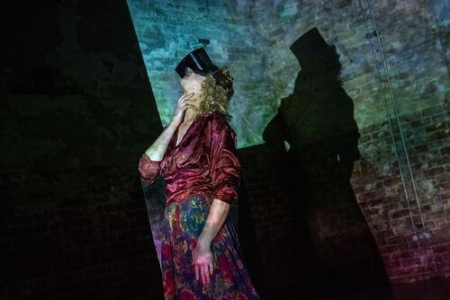 Justine Cooper with projections cast on her, wearing a VR headset and looking to the ceiling