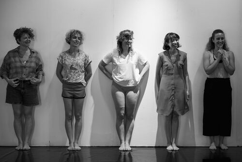 Dancers in black and white standing against a studio wall