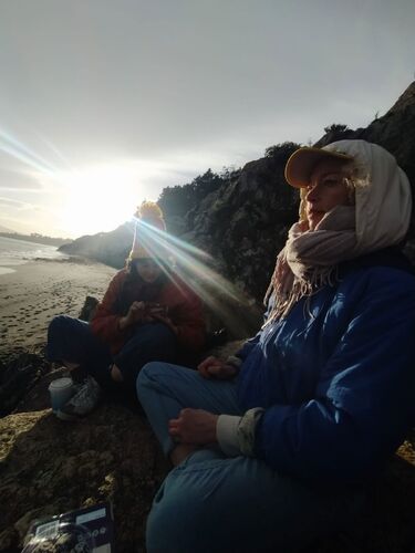 Two figures with the sun behind them sitting on a beach