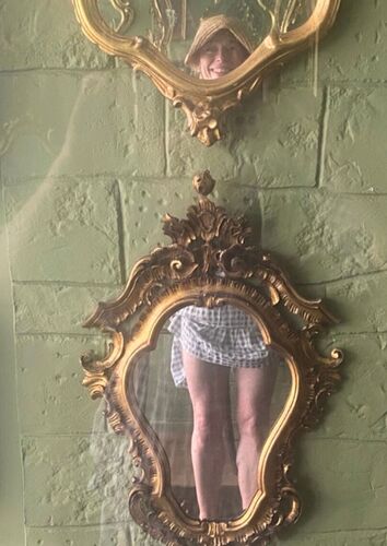 A pair of legs reflected in an ornate mirror on a wall