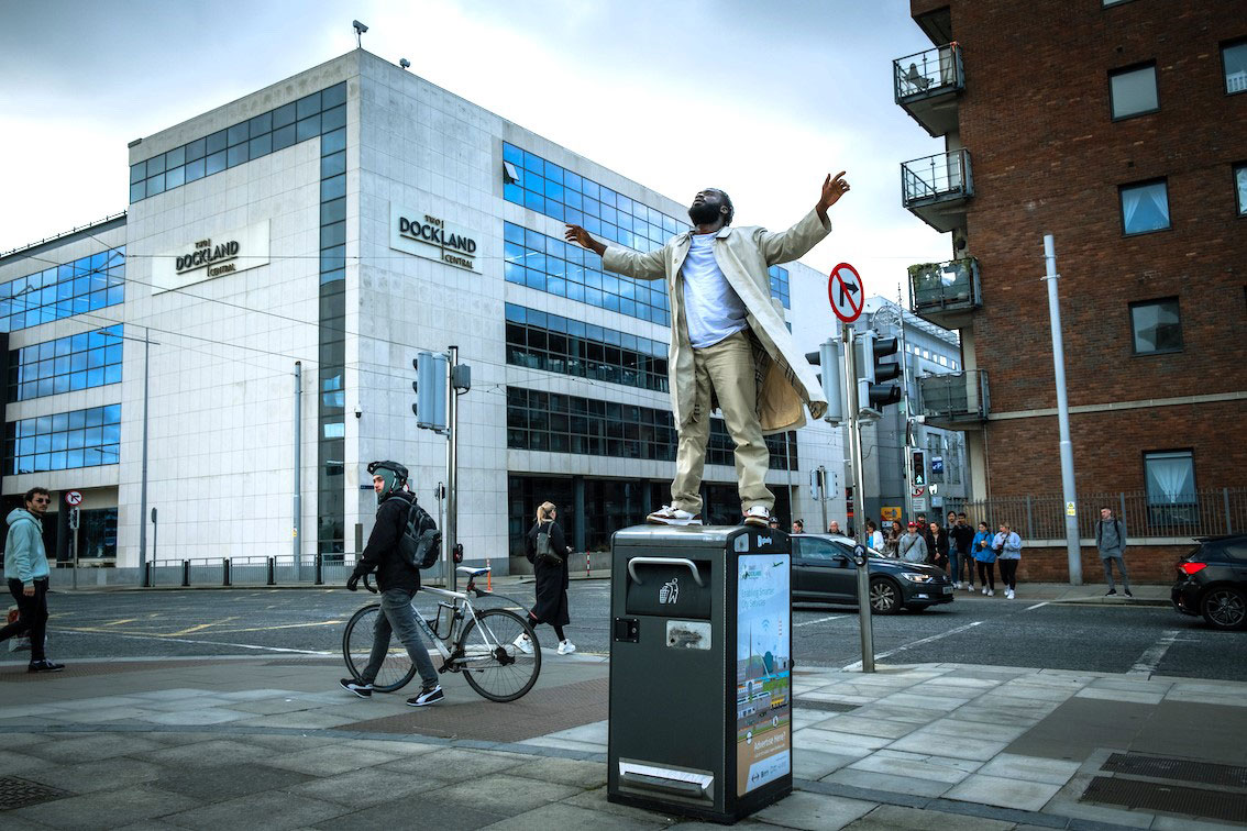 Favour Odusola standing on top of a bin at Spencer Dock with the sky behind him