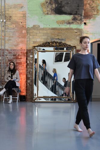 A participant in movement across the studio with others reflected in the mirror