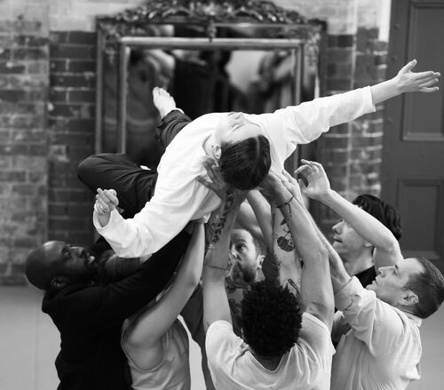 An ensemble of dancers in black and white, lifting a single dancer above their heads