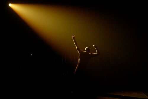 A solo dancer silhouetted in golden light on stage