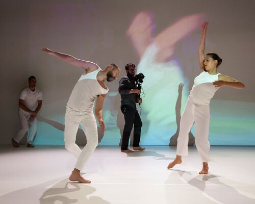 Two dancers in movement being filmed and projected live to the walls behind them
