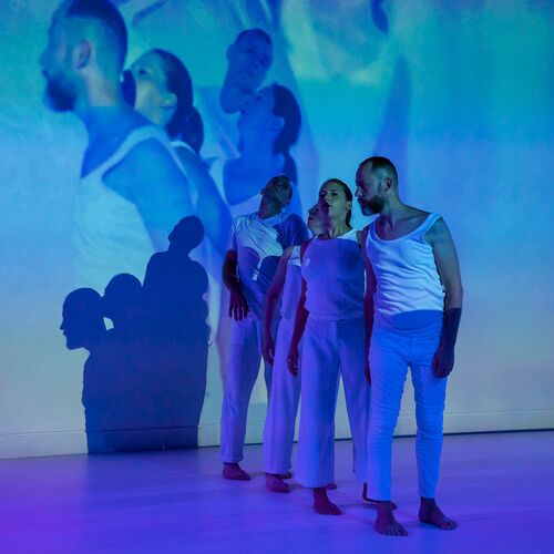 A line of four dancers cast in blue light in movement
