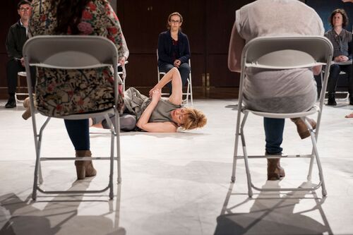 Justine Cooper in movement on the floor seen between audience chairs