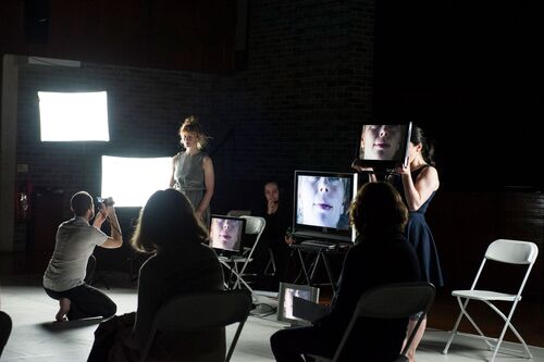 Justine Cooper standing among screens showing her face cast live from a camera feed