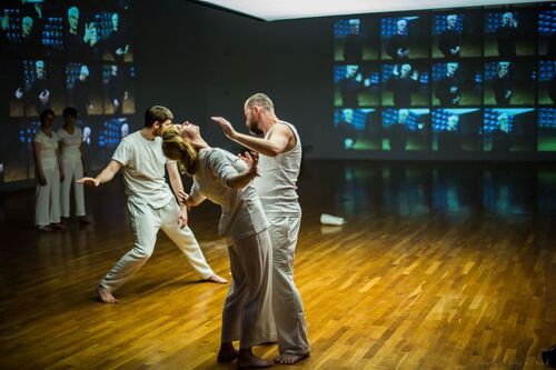Three dancers in movement lit in the centre of a gallery space