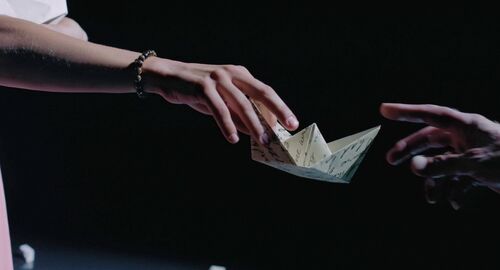 Hands passing a paper boat