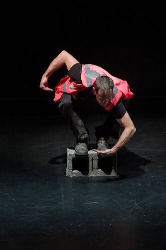 A figure in a pink hi-vis vest in movement perched on top of a cinder block