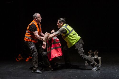 Three figures in hi-vis vests in motion lifting one in the middle by his arms