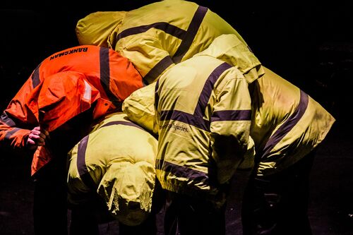 Four figures in hi-vis jackets curled around each other