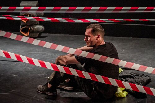 A figure sitting amid striped construction tape