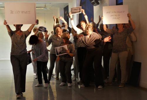 An ensemble of participants in grey holding signs and images aloft