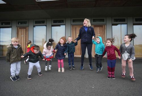 A group of children and their carer standing in line and jumping