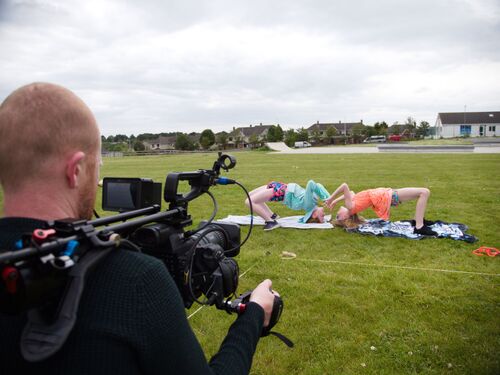 A camera filming two children doing the crab on a sports field