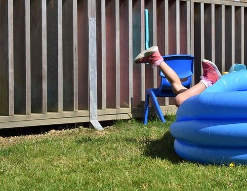 A child's legs sticking out of an empty blue inflatable paddling pool