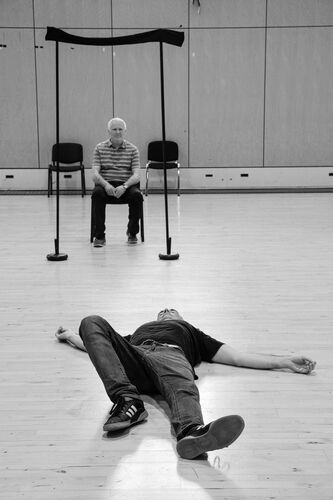 A participant lies on the floor as another participant, seated, looks on