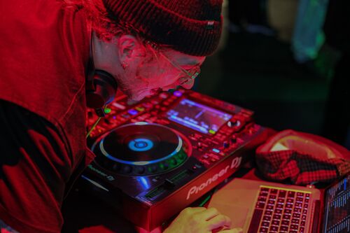 A DJ laughing bent over decks and a laptop