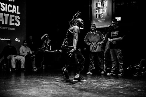 A dancer in movement with others watching on in black and white