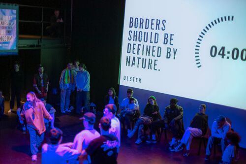 A populated dance floor with 'BORDERS SHOULD BE DEFINED BY NATURE' and a timer projected on the wall