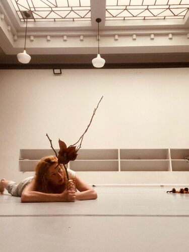 Justine Cooper lying on the floor of a studio, holding a sculpture of twigs and leaves