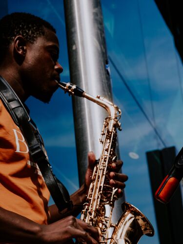 A figure in side profile playing saxophone with a blue sky in the background