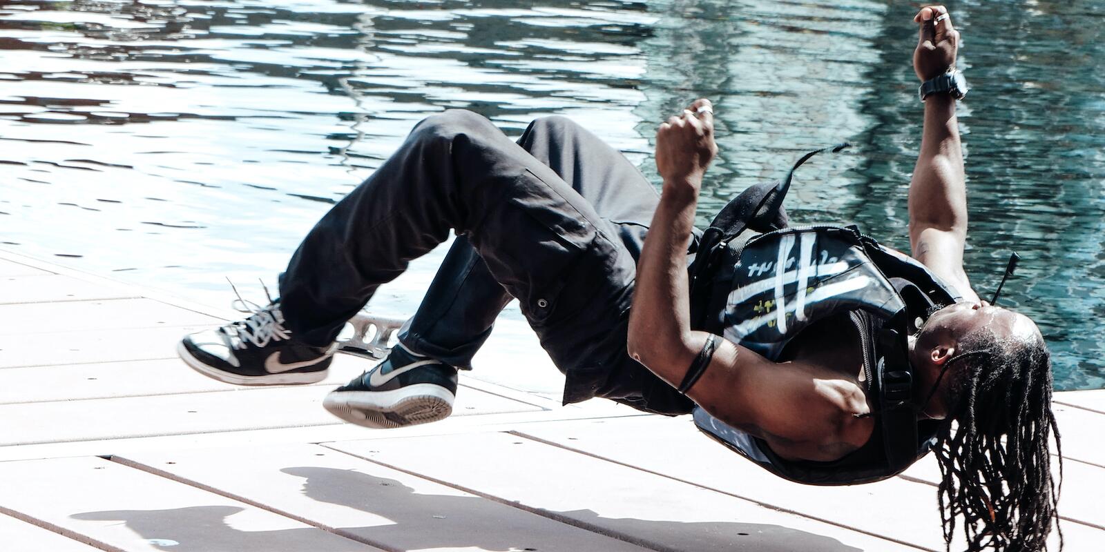 A figure lying horizontally airborne on a dock on water