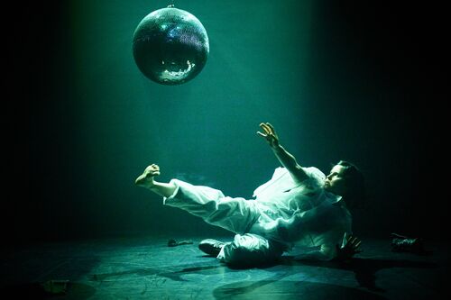 Dancer in motion lying down on the dance floor and interacting with the mirror ball