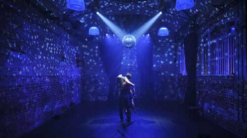 Male dancer lifting female dancer on the stage under mirror ball lights