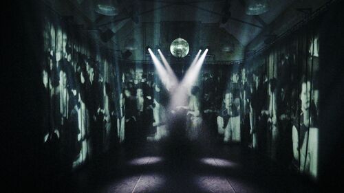 A stage with hanging mirror ball and projection of a crowd of people talking on 1950s