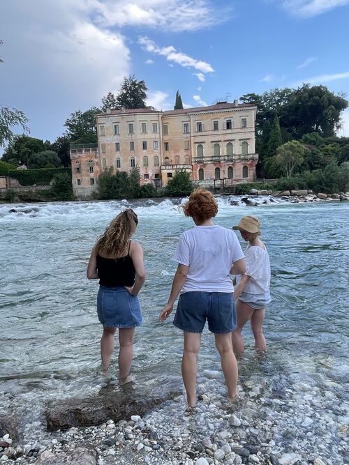 Three women with their backs in the river facing a building